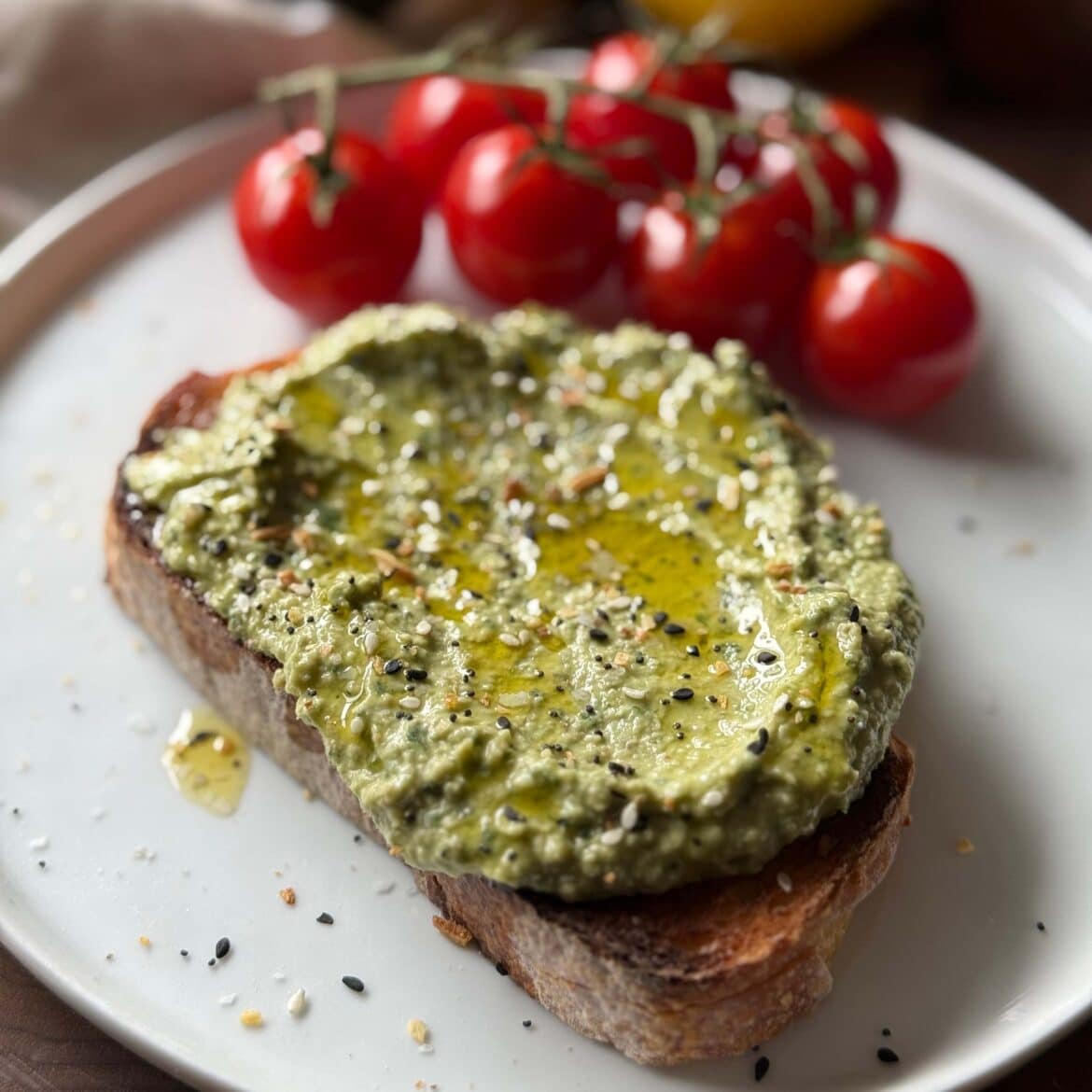 Avocado Pesto on a piece of toasted bread with a side of cherry tomatoes on the vine