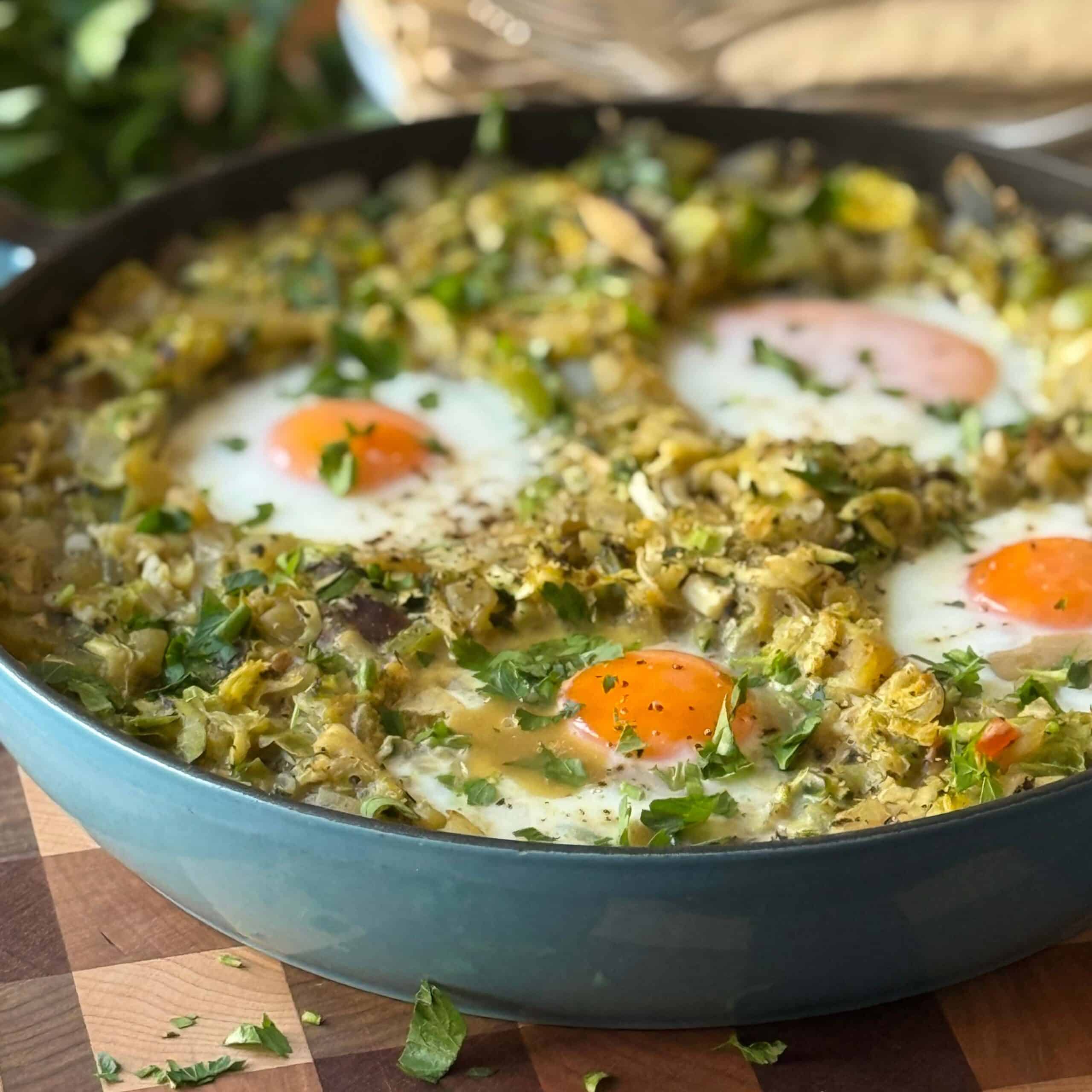 Green Shakshuka in a large pan with poached eggs on top of a mix of cooked vegetables including brussels sprouts, shredded zucchini, mushrooms and green bell peppers.