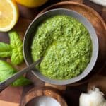 Dairy Free Pesto in a bowl with a spoon and ingredients surrounding it