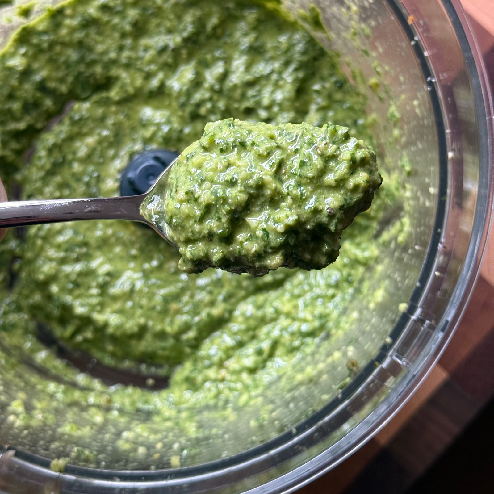A spoonful of dairy-free pesto lifted from the bowl of a food processor, showing its thick, textured consistency.