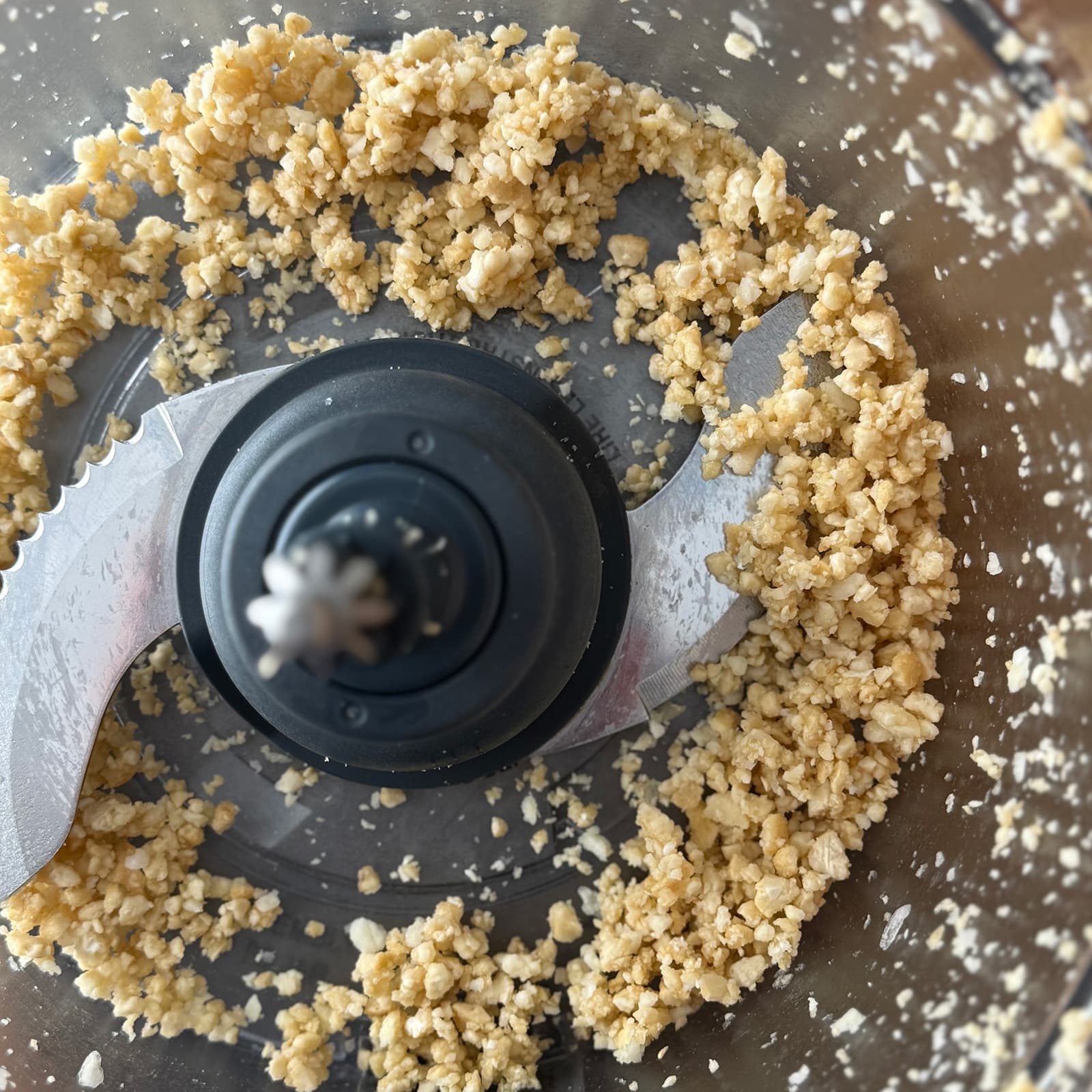 Minced cashews and garlic in a food processor bowl, forming the base for carrot top pesto