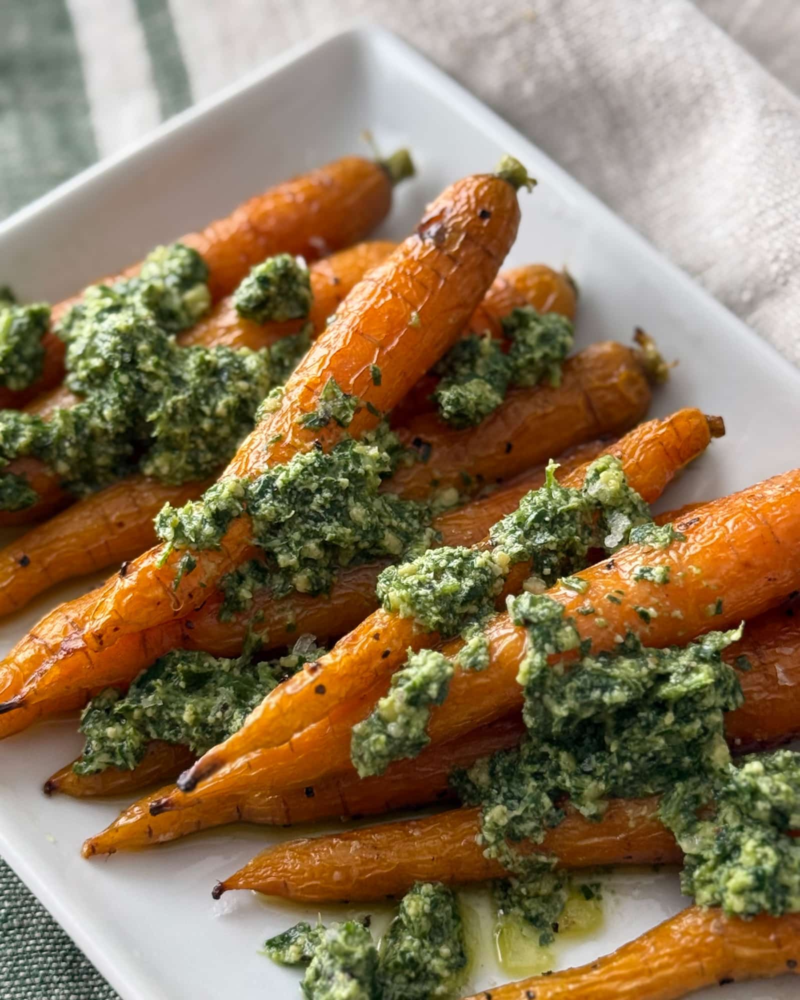 Roasted carrots on a white plate topped with spoonfuls of carrot top pesto