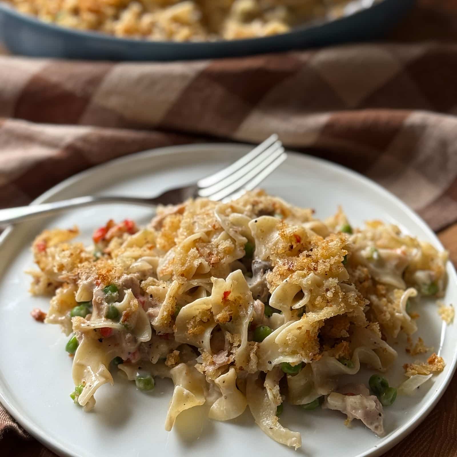 A plate of tuna noodle casserole with peas and a crispy breadcrumb topping, served with a fork