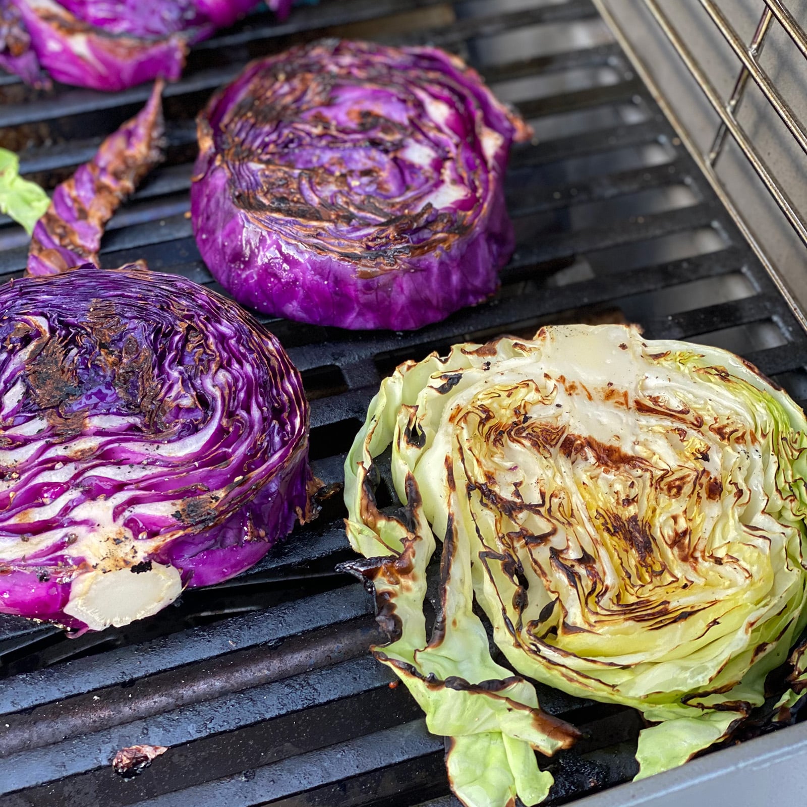 Red and green cabbage steaks on a hot gas grill with visible char marks and caramelized edges.