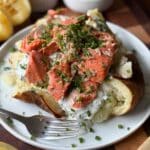 Roasted salmon sits on top of a cut-open baked potato with sour cream sauce