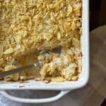Funeral Potatoes (Cheesy Potato Casserole) is scooped onto a spoon resting in the corner of a baking dish.