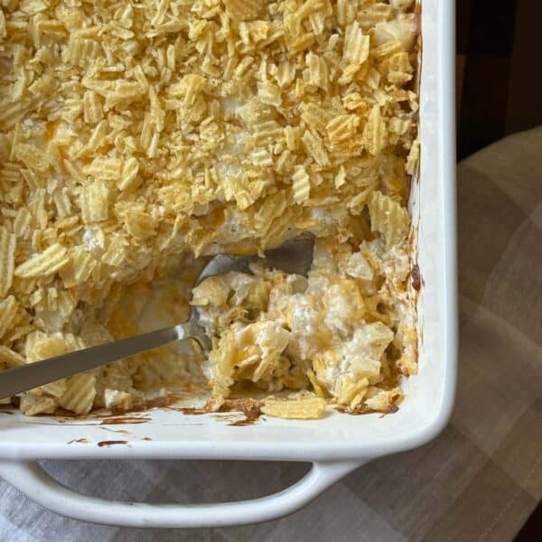 Funeral Potatoes (Cheesy Potato Casserole) is scooped onto a spoon resting in the corner of a baking dish.