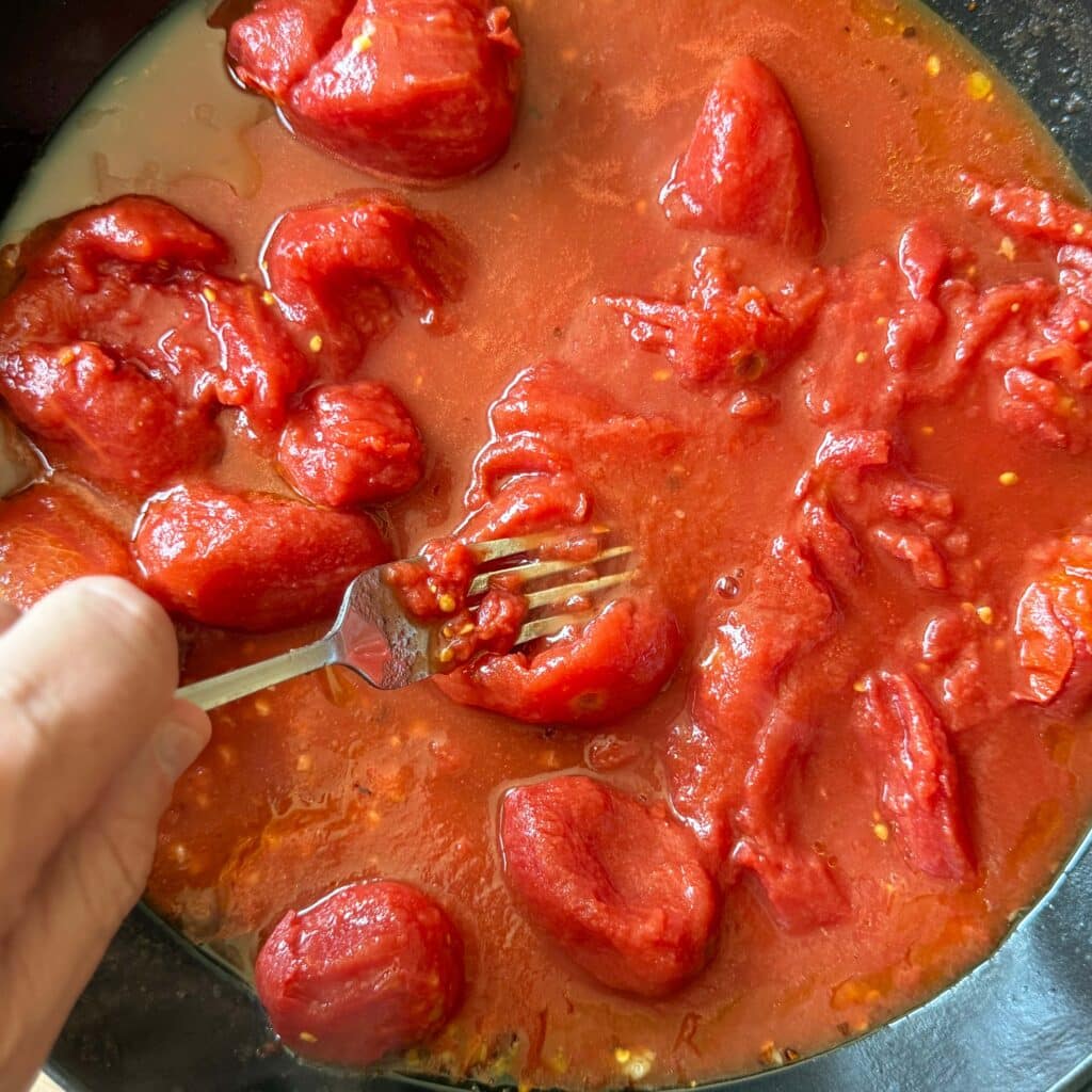 Smashing Whole Peeled Tomatoes with a Fork in Skillet