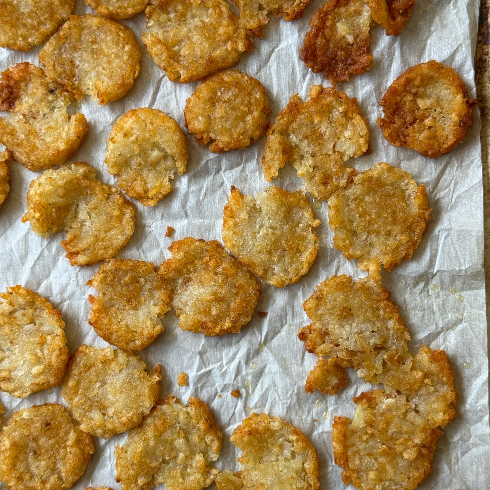 Golden, crispy smashed tater tots on a parchment-lined baking sheet after baking at 425 degrees.