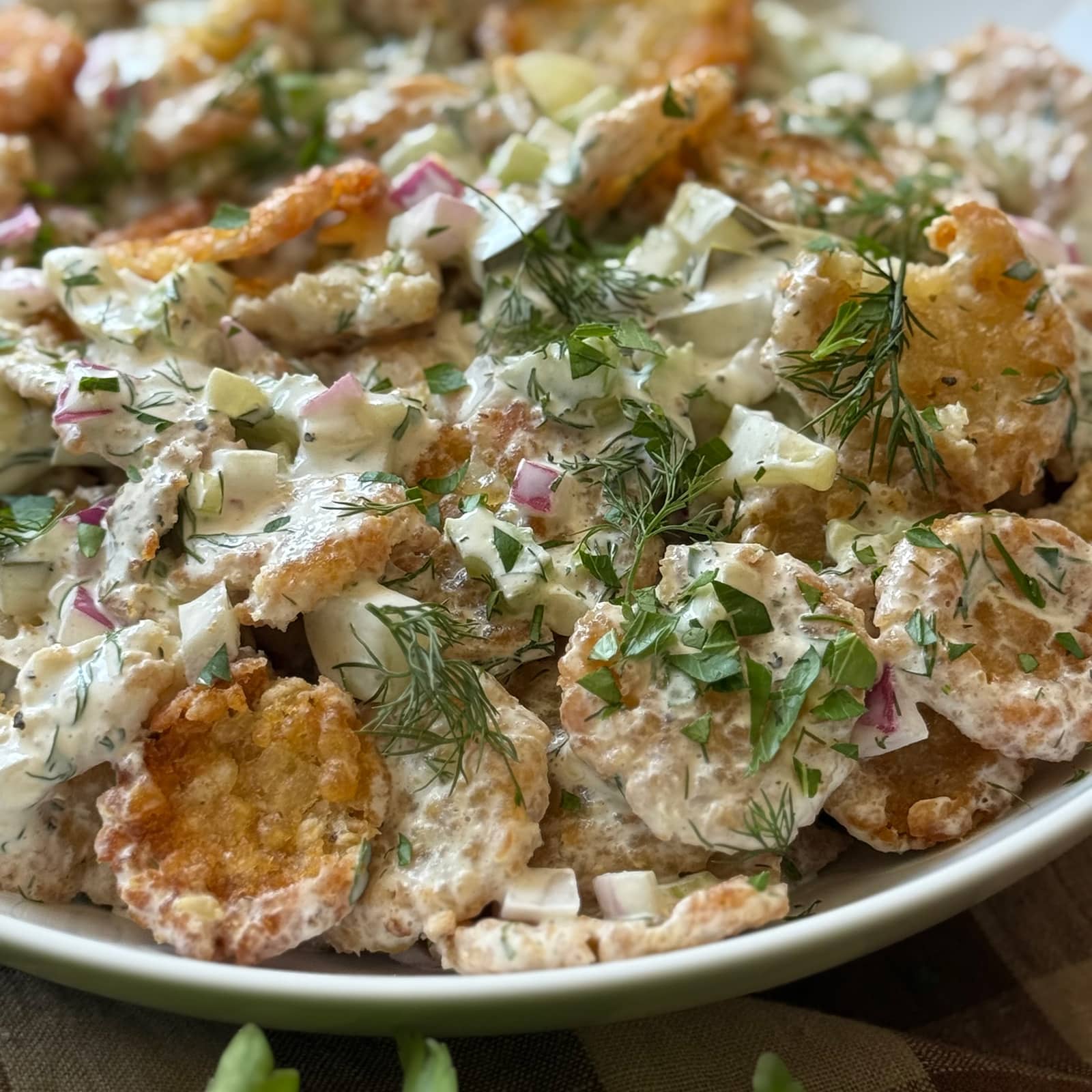 Close-up of crispy tater tot potato salad garnished with fresh dill sprigs and chopped parsley, showing golden crispy tater crown edges coated in creamy herb dressing.