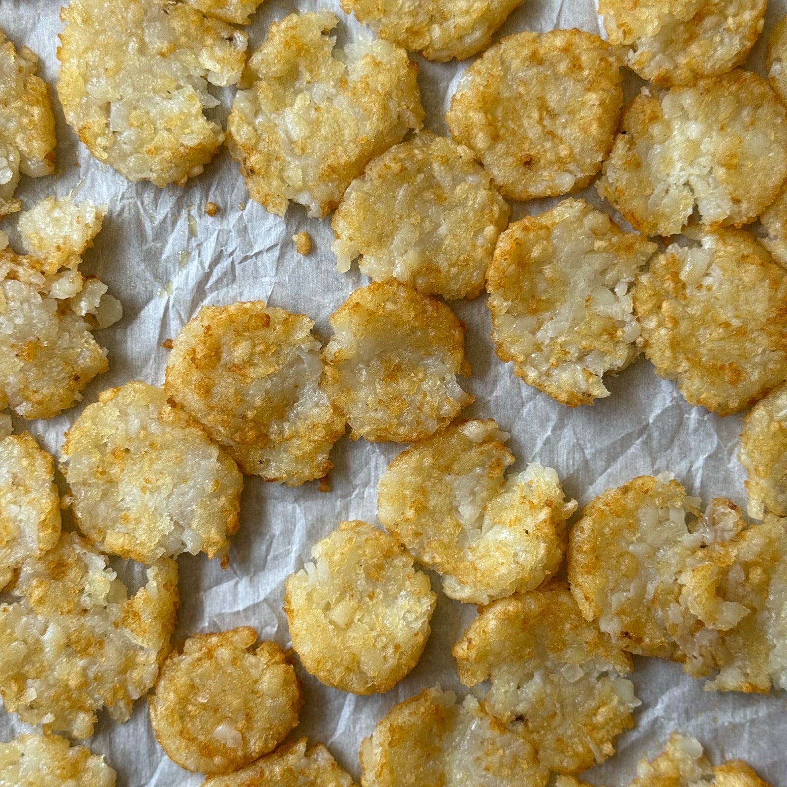 Smashed tater tots pressed into flat discs on a parchment-lined baking sheet, ready for the second bake.