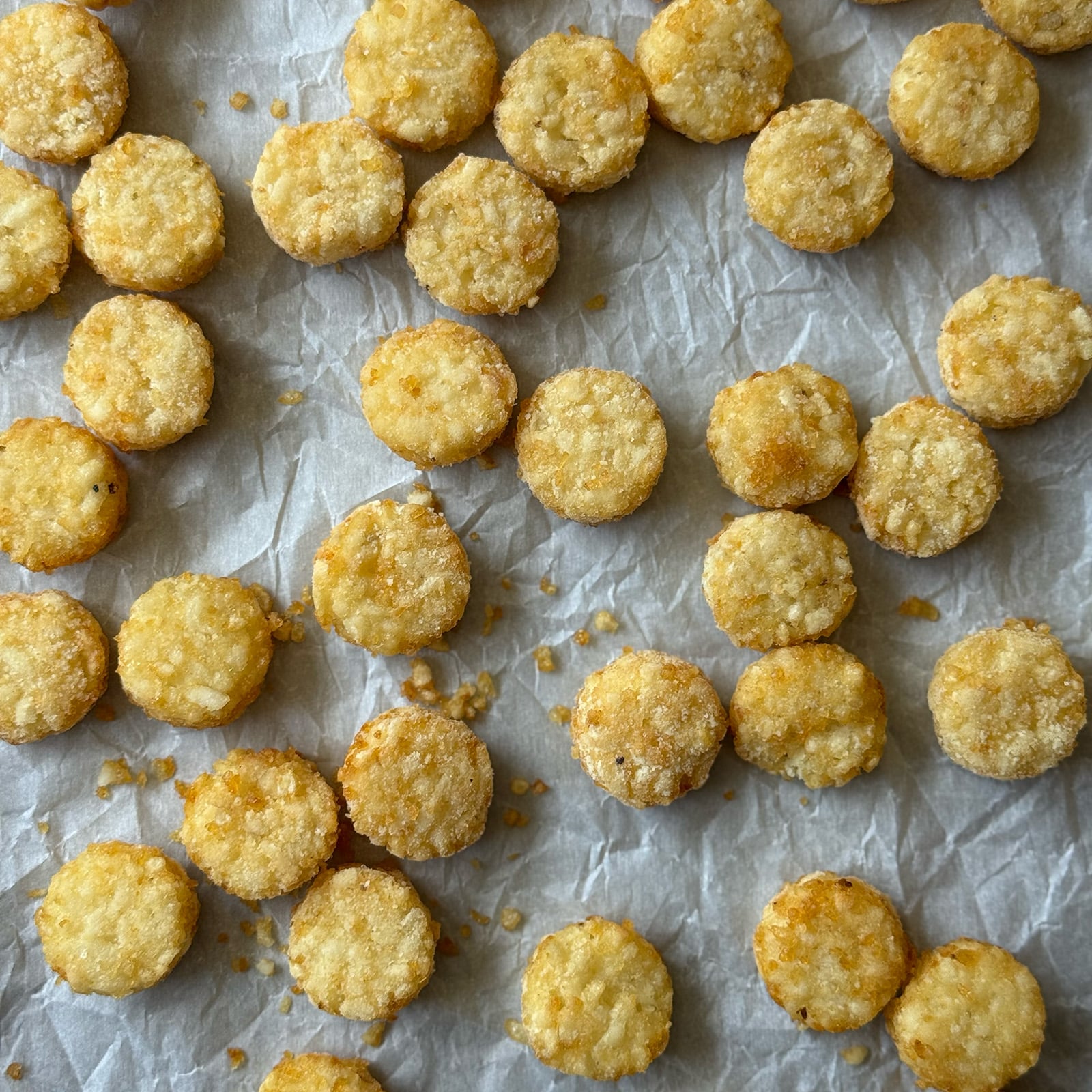 Frozen tater crowns spread in a single layer on a parchment-lined baking sheet before baking.