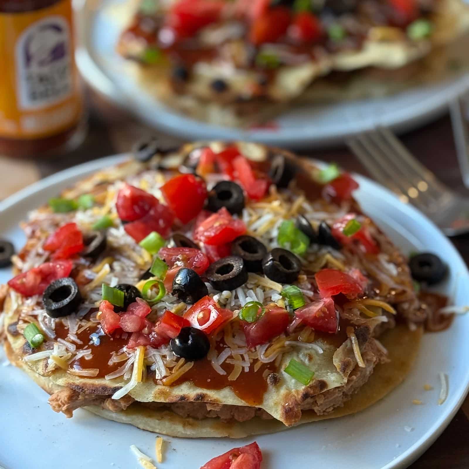 Vegetarian Mexican pizza on a white plate topped with diced tomatoes, black olives, and green onions.