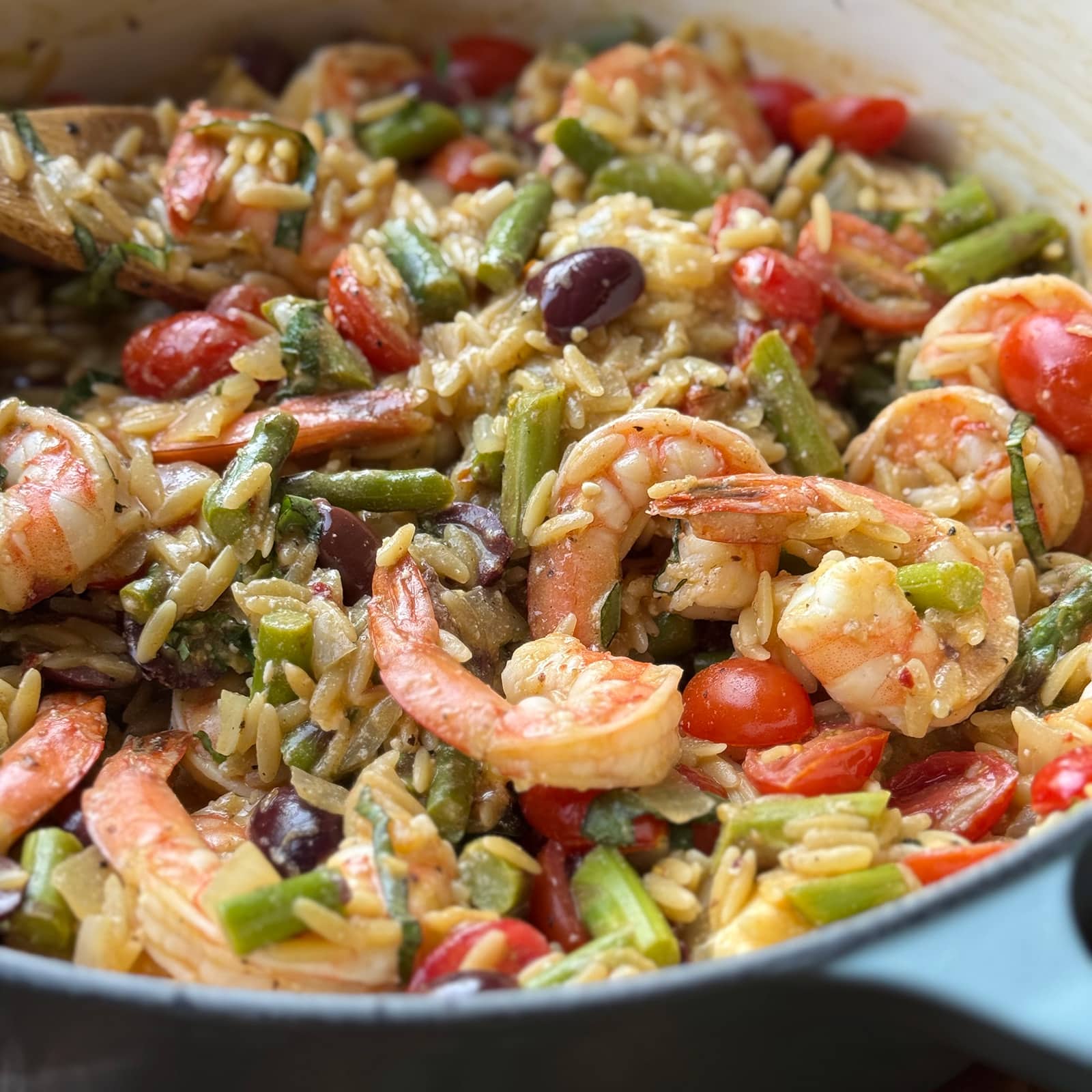 closeup of shrimp and orzo in a pot with asparagus, tomato, and olives