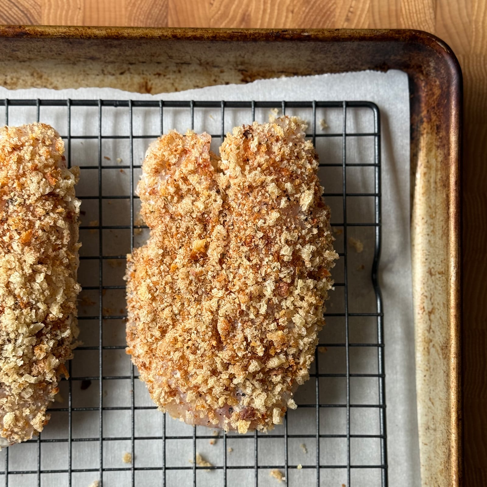 Two Cajun panko-breaded tilapia fillets on a wire rack set over a parchment-lined baking sheet ready to go into the oven