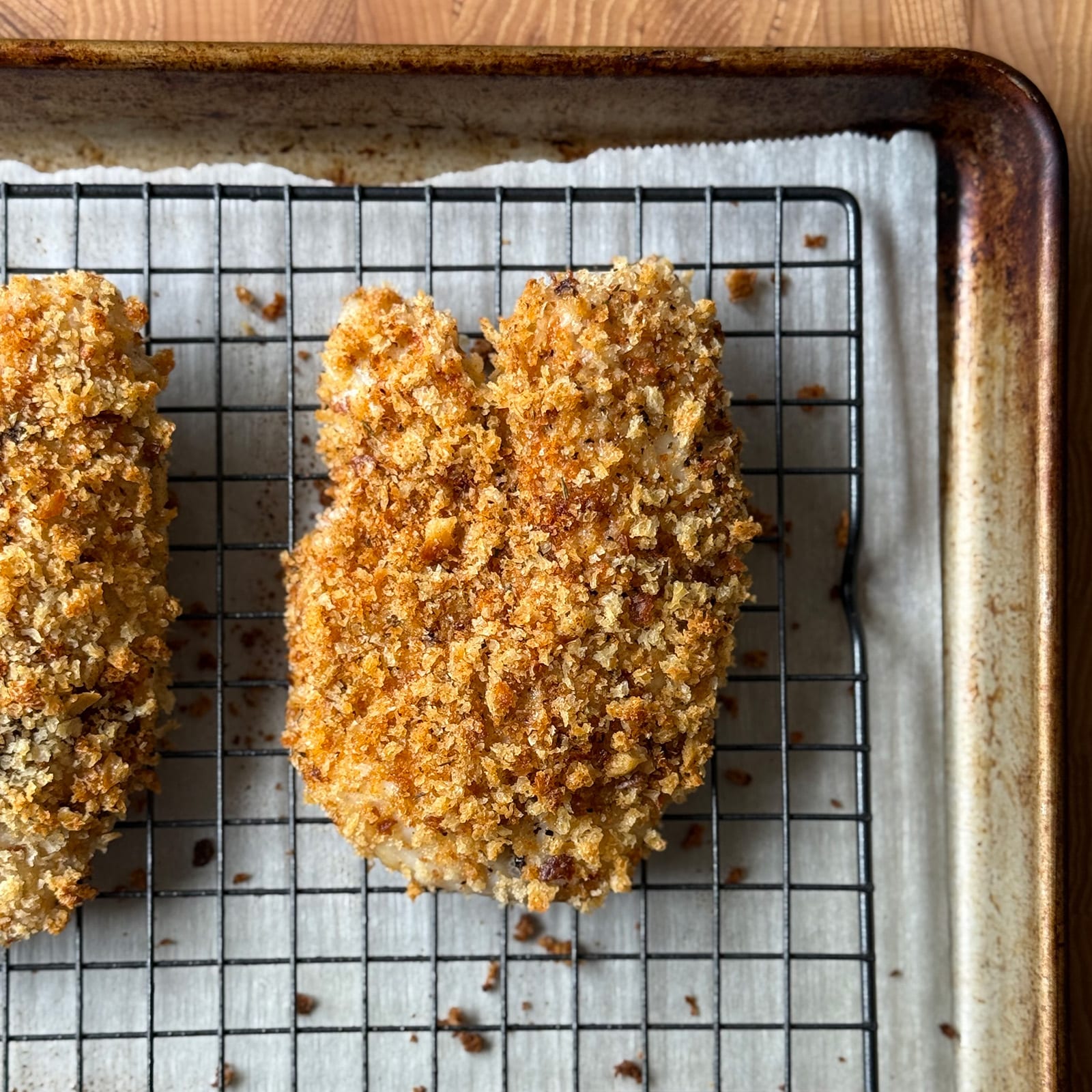 Two crispy golden Cajun breaded tilapia fillets fresh from the oven on a wire rack over a parchment-lined baking sheet