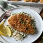 Crispy cajun breaded tilapia fillet served over basmati rice with fresh herbs and lemon wedges on a white plate