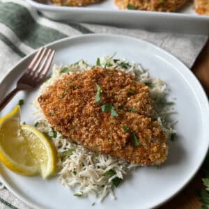 Crispy cajun breaded tilapia fillet served over basmati rice with fresh herbs and lemon wedges on a white plate