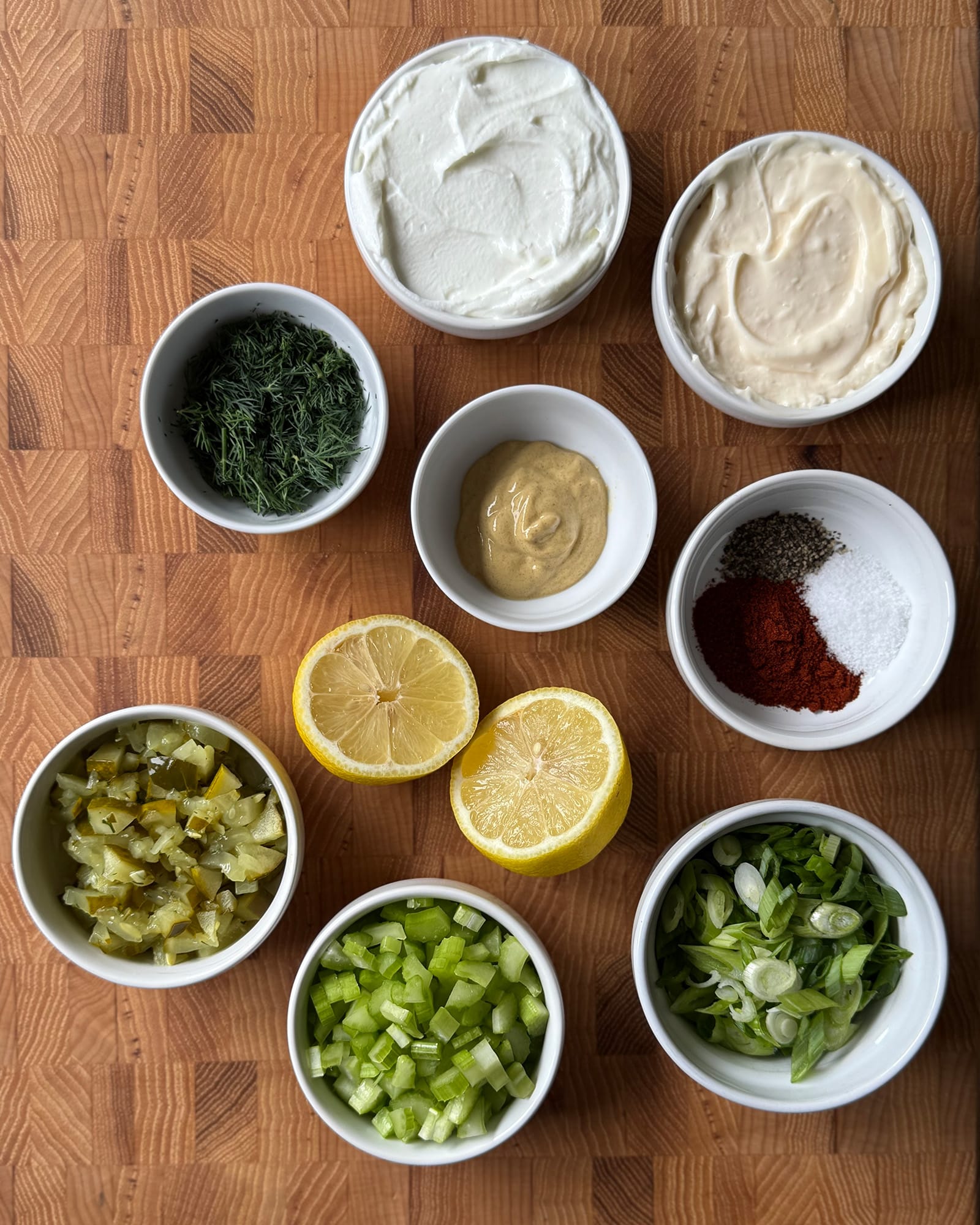 Ingredients for smashed sweet potato tater tot salad including fresh dill, chopped dill pickles, diced celery, sliced green onions, a halved lemon, Dijon musta&hellip;Ingredients for smashed sweet potato tater tot salad including fresh dill, chopped dill pickles, diced celery, sliced green onions, a halved lemon, Dijon mustard, mayonnaise, plain Greek yogurt, and a small bowl of smoked paprika, salt, and black pepper arranged on a butcher block cutting board.