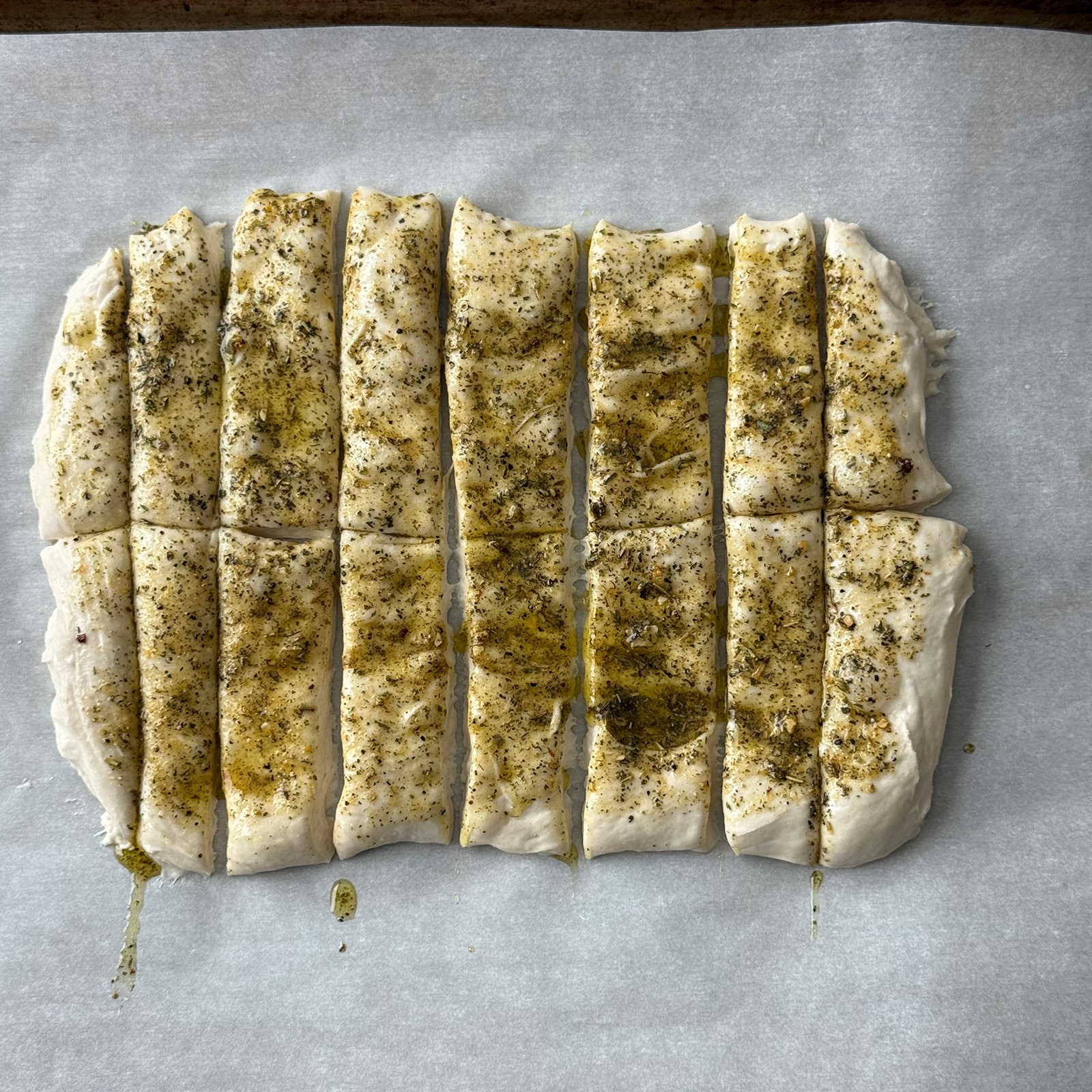Pizza dough brushed with Italian seasoning mixture and cut into strips with a pizza cutter, ready to bake.