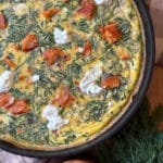 Overhead view of a smoked salmon frittata in an ovenproof skillet with goat cheese, fresh dill, and flaked smoked salmon