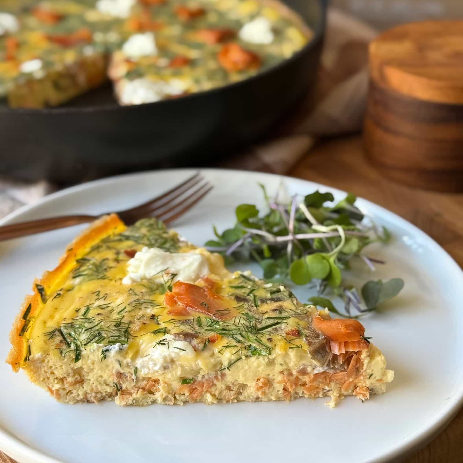 A slice of smoked salmon frittata on a white plate with microgreens