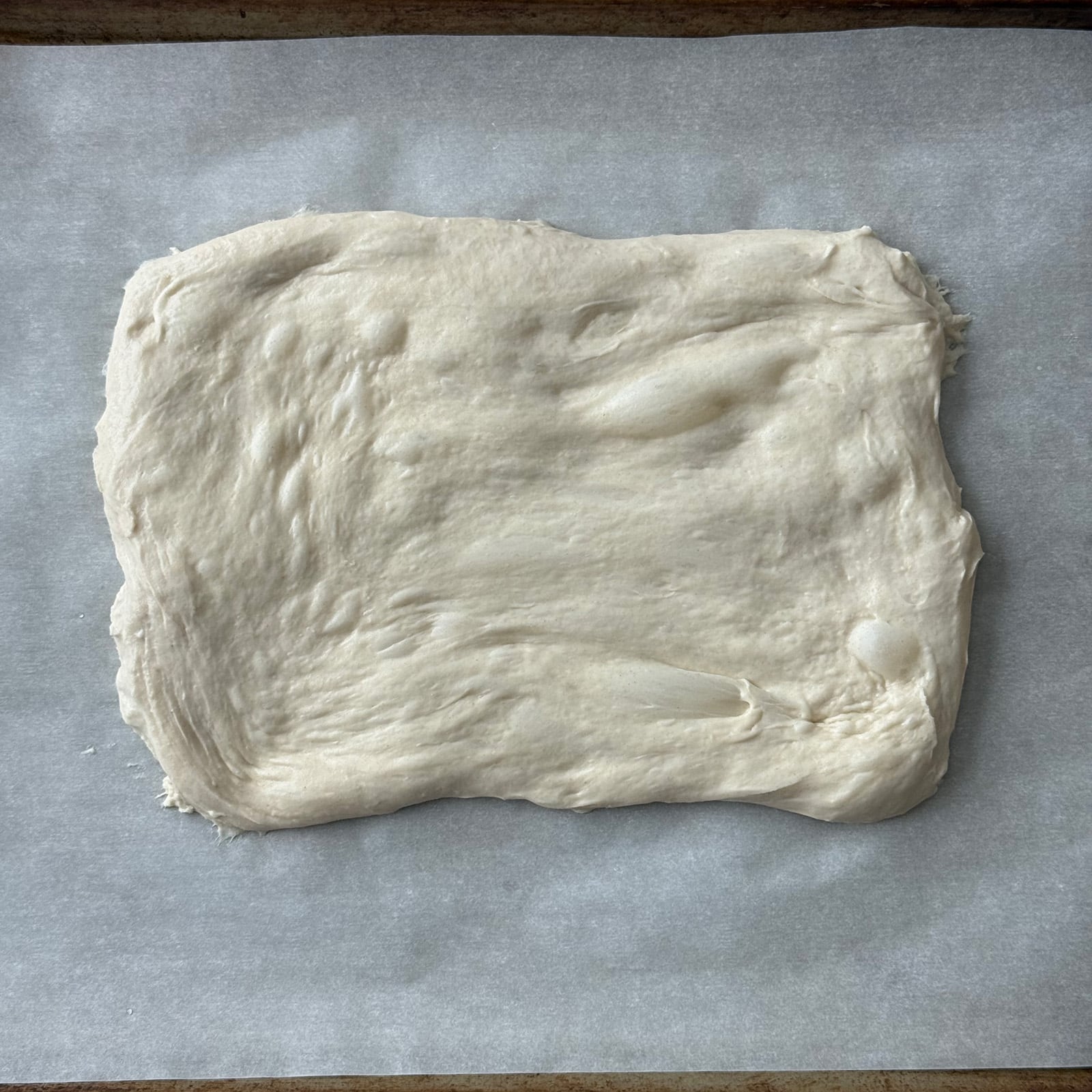Pizza dough stretched into a rectangle on a parchment-lined baking sheet.