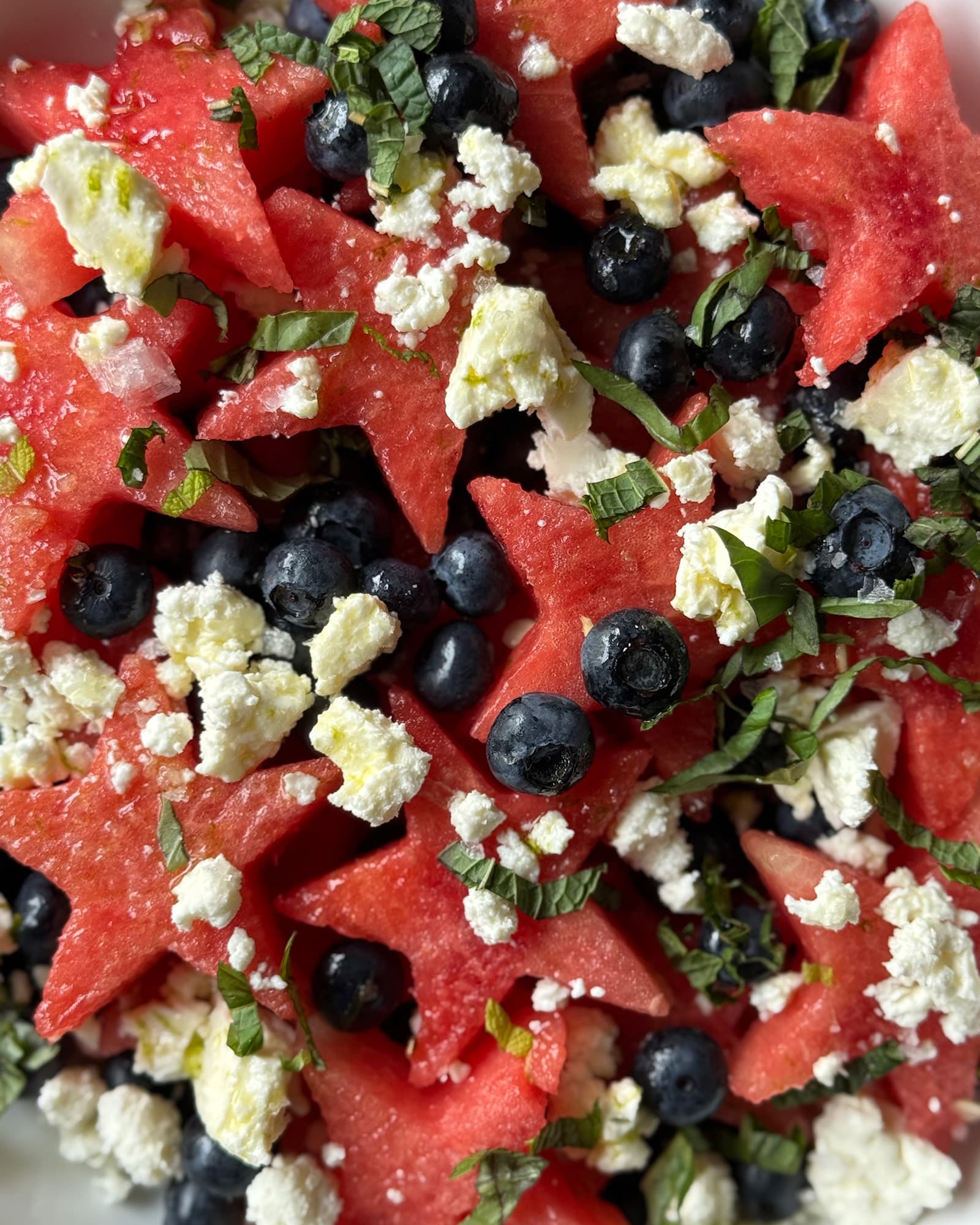 A close-up overhead view of watermelon blueberry salad with crumbled feta and fresh chopped basil and mint.