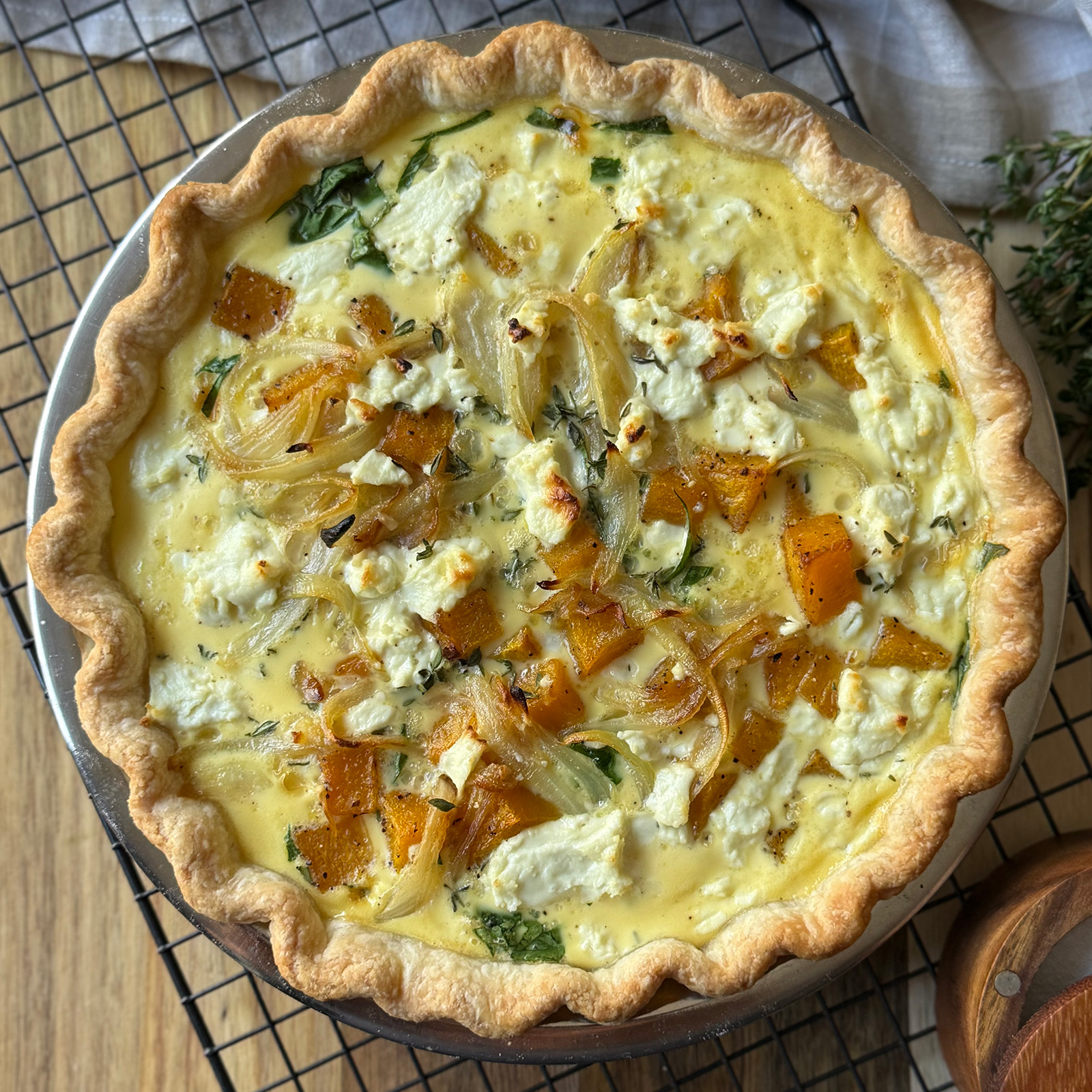 A golden butternut squash quiche filled with roasted butternut squash, caramelized onions, spinach, and crumbled goat cheese, in a flaky crust, rests on a cooling rack.
