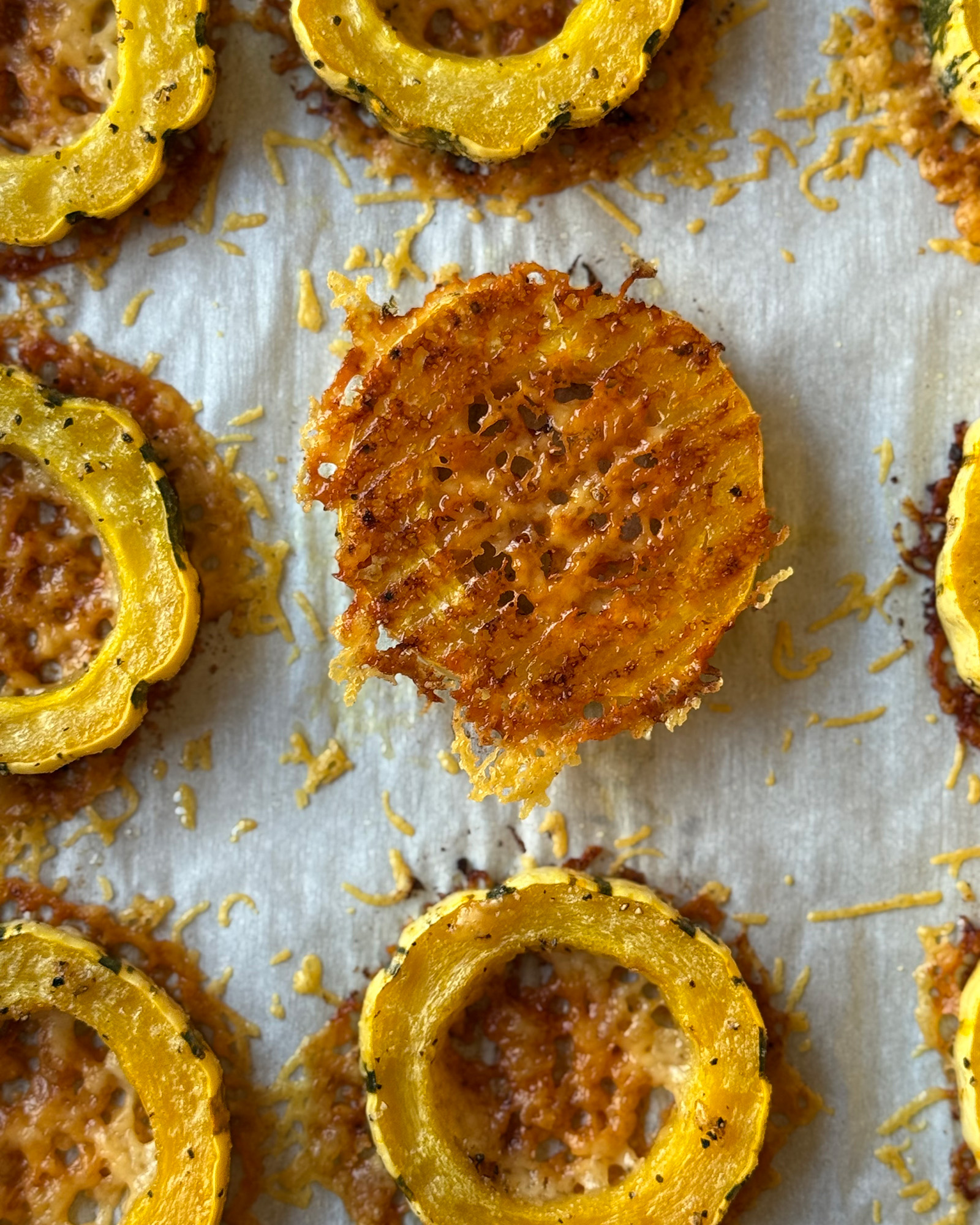 Baked delicata squash rings on parchment, with one flipped over to show a crispy, golden Parmesan crust.