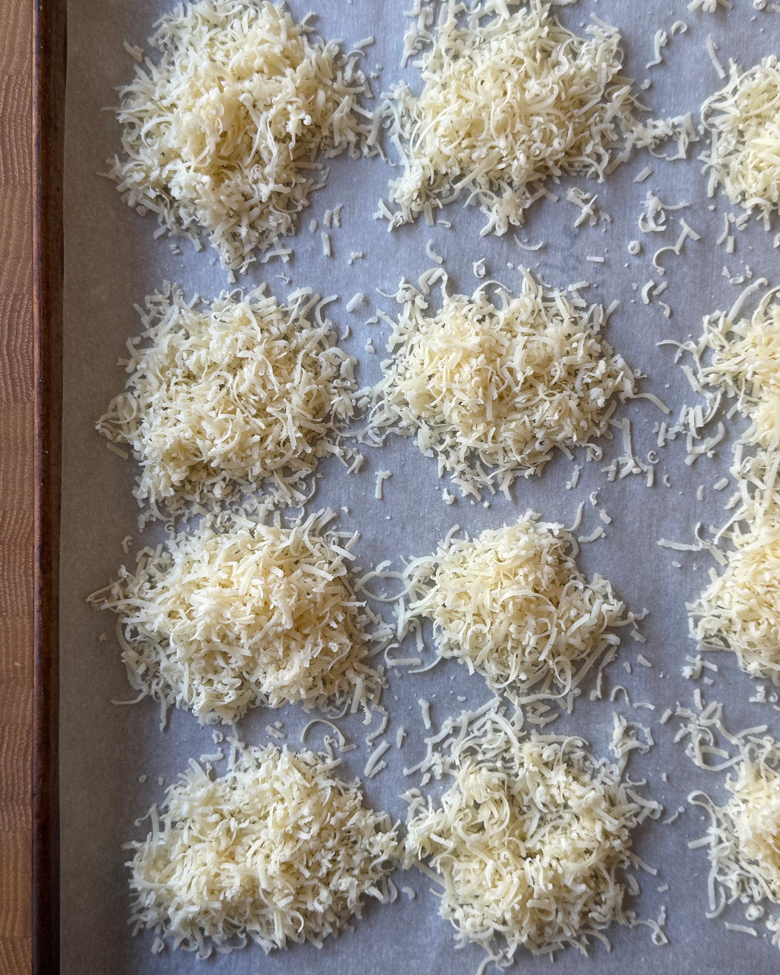 Mounds of freshly grated Parmesan spaced in rows on a parchment-lined baking sheet.