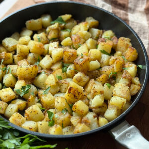 A skillet filled with golden-brown diced potatoes seasoned with herbs.