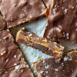 Square chocolate-covered bars topped with sea salt, with one piece turned on its side to show a date and peanut filling.