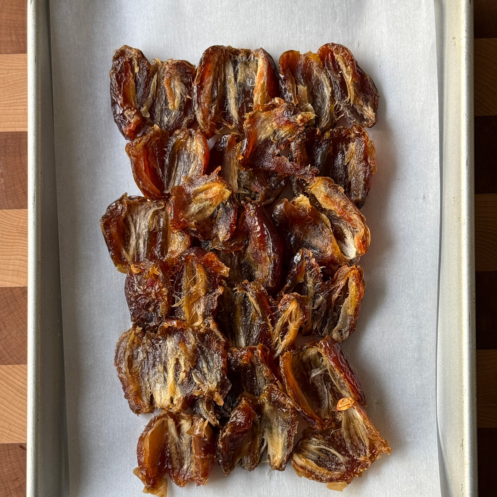 Split Medjool dates arranged cut side up in rows on a parchment-lined sheet pan.