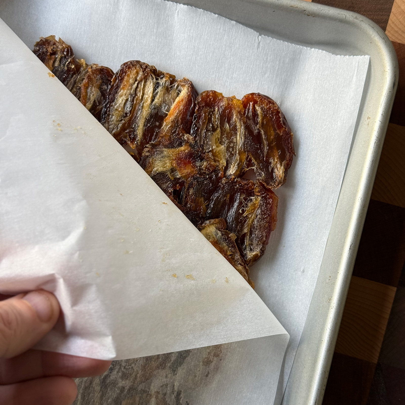Hand peeling back a sheet of parchment paper to reveal dates pressed into a flat layer.