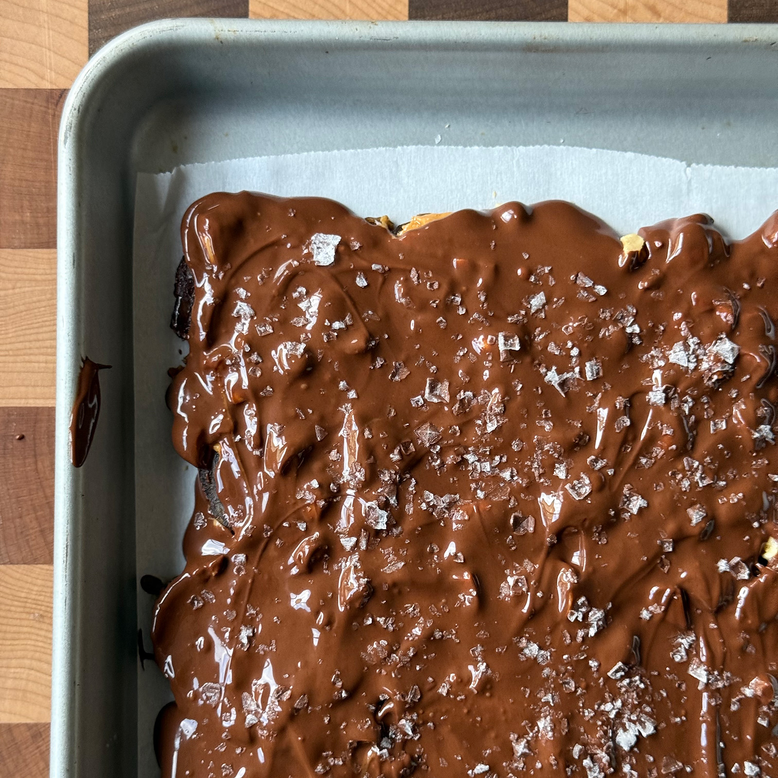 Smooth chocolate layer topped with flaky sea salt on a parchment-lined sheet pan.