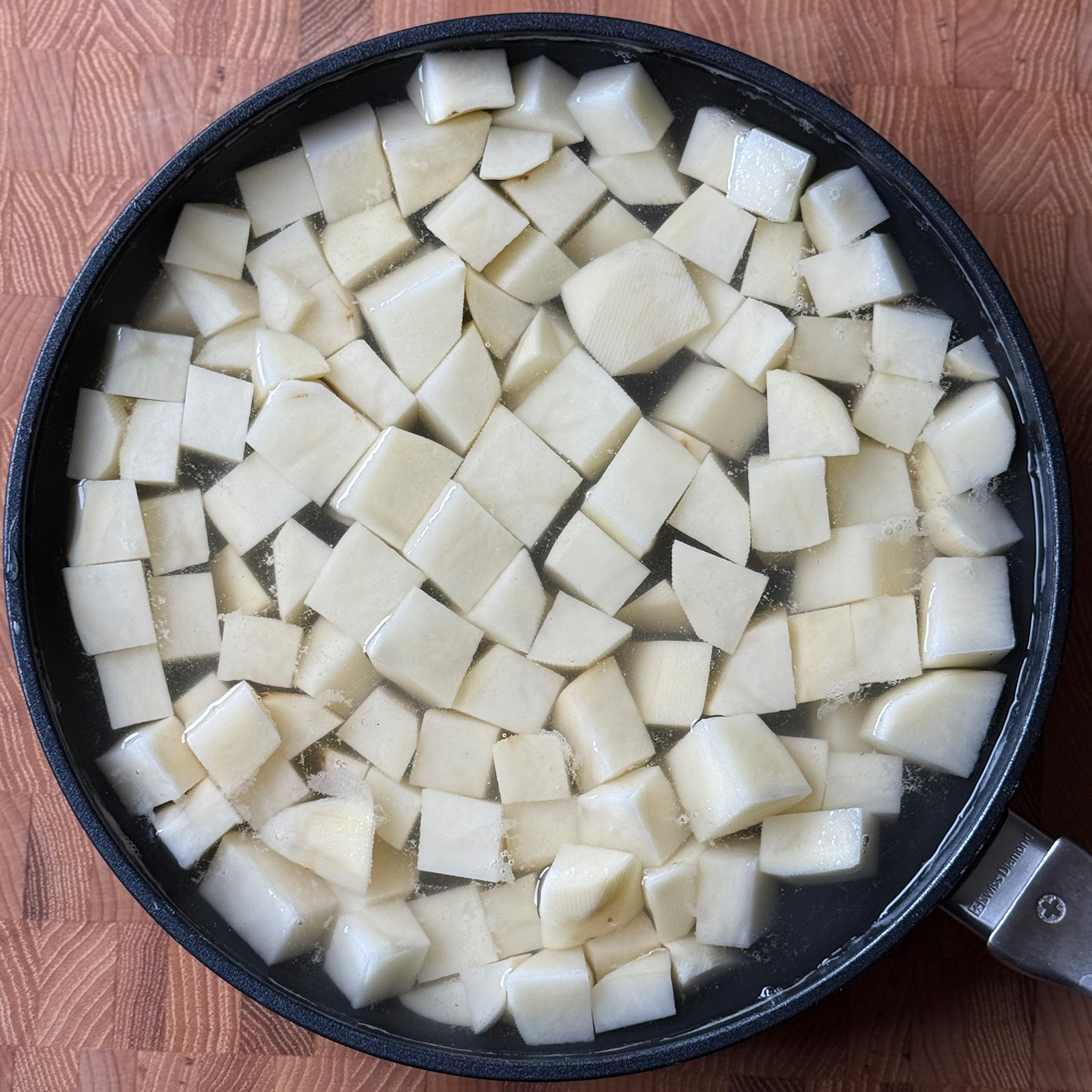 Peeled and cubed russet potatoes covered with cold water in a large skillet before boiling.